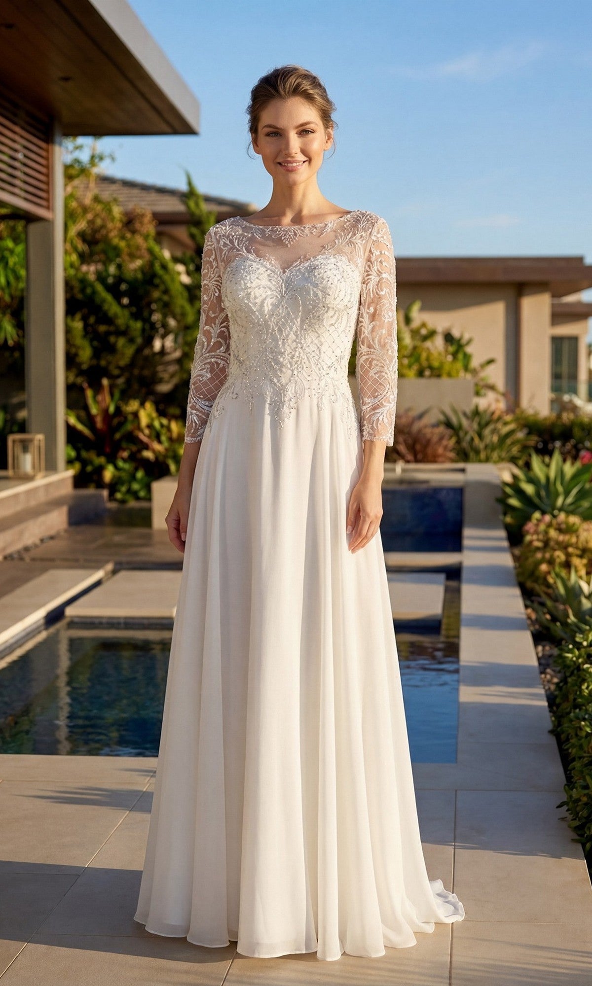 A woman stands outdoors near a pool, surrounded by greenery, wearing the Long Formal Dress: Juliet M11-W—a white wedding gown featuring lace sleeves and an embroidered bodice.